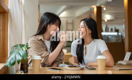 Zwei schöne und glückliche asiatische Frauen genießen eine lustige Zeit zusammen in einem Coffee Shop, genießen ein Dessert und unterhalten sich lebhaft. Ein Freund Stockfoto