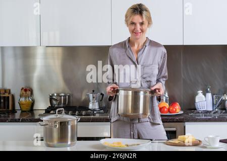 Frau steht neben Tisch in der Küche zu Hause. Hausfrau kocht morgens in der Küche. Stockfoto