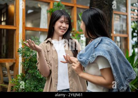 Zwei fröhliche asiatische Freundinnen unterhalten sich beim Spaziergang durch einen Garten. Klatsch, plaudernd, redend Stockfoto