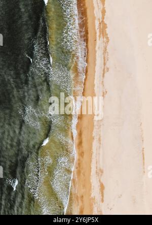 Aus der Vogelperspektive auf Meereswellen, die sanft auf einen Sandstrand gleiten, bilden einen wunderschönen Kontrast zwischen dem Wasser und dem Ufer. Stockfoto