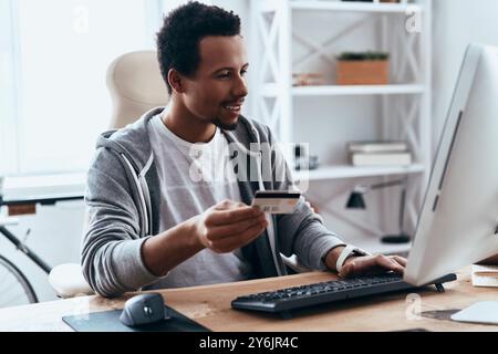 Etwas bestellen. Glücklicher junger Mann in lässiger Kleidung, der online kauft, während er Zeit zu Hause verbringt Stockfoto