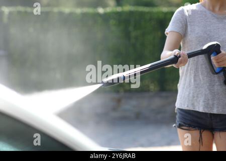 Nahaufnahme einer Frau, die das Auto mit Wasser wäscht, mit Hochdruckreiniger im Garten zu Hause Stockfoto