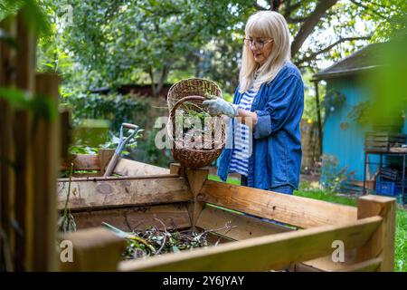 Eine ältere Frau wirft Gemüseabfälle in einen Komposthaufen im Garten Stockfoto