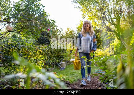 Reife Frau, die an einem sonnigen Sommertag Pflanzen in ihrem Garten gießt Stockfoto