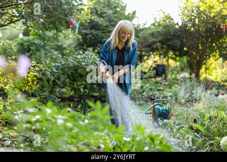 Reife Frau, die an einem sonnigen Sommertag Pflanzen in ihrem Garten gießt Stockfoto