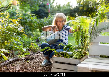 Reife Frau, die an einem sonnigen Sommertag Pflanzen in ihrem Garten gießt Stockfoto