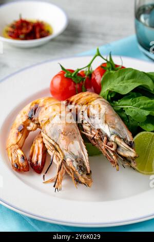 Rote Garnelen oder Tigergarnelen auf einem weißen Teller mit Gemüse und Tomaten. Tigergarnelen Stockfoto
