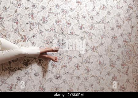 Nahaufnahme eines wunderschönen persischen Teppichs mit Blumenmustern, der einen entspannten Moment mit Blick auf die Beine einer Person zeigt Stockfoto