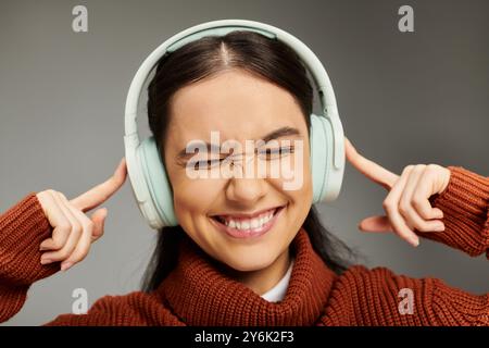 Eine junge Frau hört fröhlich Musik, trägt Kopfhörer und präsentiert ihr stilvolles Outfit. Stockfoto