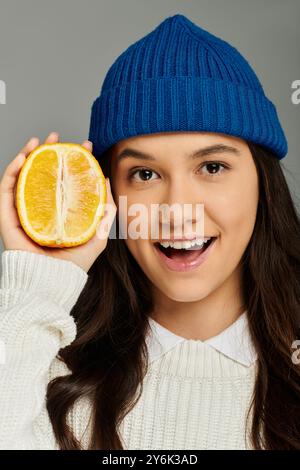 Eine junge Frau hält fröhlich ein frisches Orange, das ihren verspielten Geist und Stil unterstreicht. Stockfoto