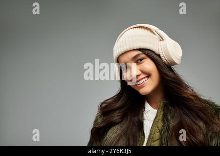 Eine lebendige junge Frau mit einem warmen Lächeln genießt Musik, während sie modische Winterkleidung trägt. Stockfoto