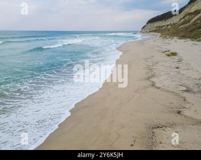 Eine ruhige Küstenszene mit türkisfarbenen Wellen, die sanft auf einen Sandstrand gleiten, umgeben von zerklüfteten Klippen. Perfekt für Natur, Reisen oder Meereslandschaft Stockfoto