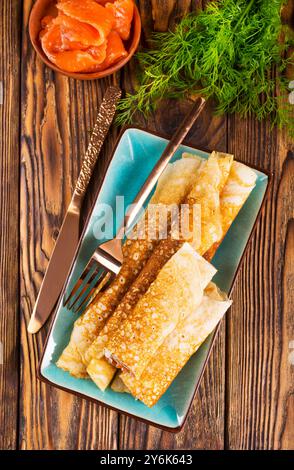 Dünne Pfannkuchen oder Crepes mit Räucherlachs und Dill auf dunklem Holzhintergrund. Selektiver Fokus Stockfoto