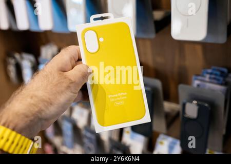 Paris, Frankreich - 20. September 2024: Eine männliche Hand hält die neueste gelbe Silikon-Hülle iPhone 16 Plus mit MagSafe in einem Apple Store, mit Hüllen dahinter Stockfoto