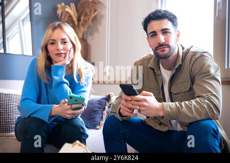 Ein Paar sitzt auf einem bequemen Sofa, jedes mit seinem Smartphone in der Hand Stockfoto