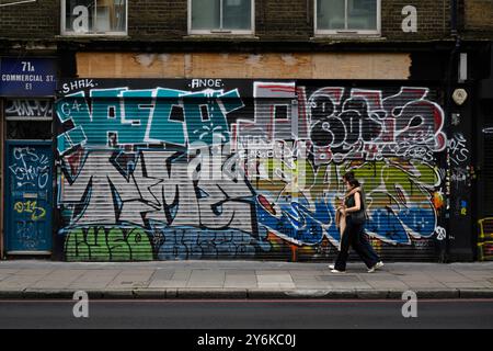 Leute, die an einer graffierten Rolltür vorbeilaufen, Commercial Street, London, Großbritannien. September 2024 Stockfoto