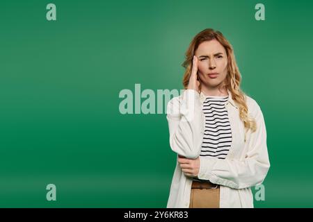 Eine lässige Frau mit schönen lockigen Haaren steht nachdenklich auf einem hellgrünen Hintergrund, verloren in ihren Gedanken. Stockfoto