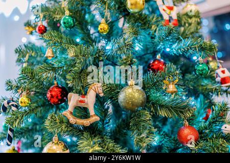 Die Figur eines Pferdes auf Läufern hängt zwischen goldenen, roten und grünen Kugeln an einem Weihnachtsbaum Stockfoto