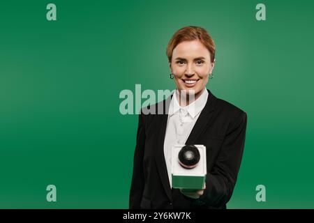 Ein selbstbewusster Fernsehmoderator in eleganter schwarzer Kleidung steht vor einem leuchtend grünen Hintergrund und begeistert die Zuschauer mit Charisma. Stockfoto