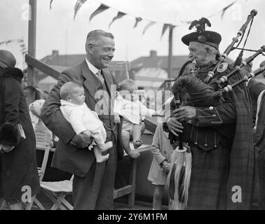 Babyshow in Chadwell Heath, in der Nähe von Barking und Dagenham, East London. Sir George Hamilton, 1. Baronet, konservatives parlamentsmitglied von Ilford mit zwei Zwillingen. Ein Hochlandpfeifer. Eastment, Stockfoto