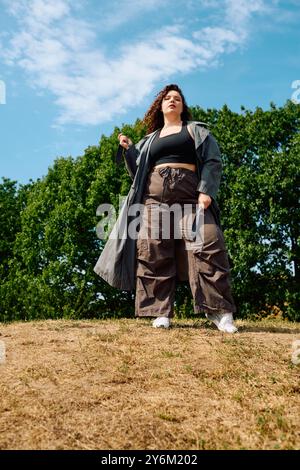 Eine stilvolle Frau in Übergröße posiert souverän inmitten üppiger Grünflächen und genießt ihre einzigartige Schönheit. Stockfoto