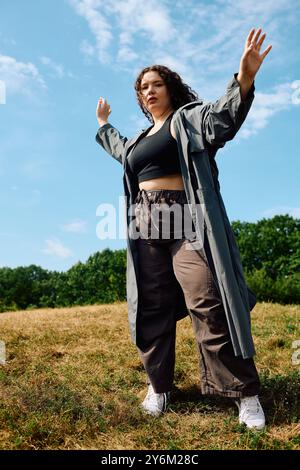 Eine Frau in Übergröße begrüßt die Freiheit und tanzt fröhlich auf einem lebendigen, sonnendurchfluteten Feld unter dem blauen Himmel. Stockfoto