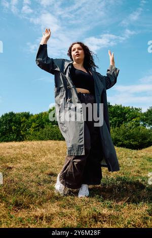 Eine selbstbewusste Frau umarmt die Natur und tanzt mit Freude auf einem offenen Feld unter sonnigem Himmel. Stockfoto