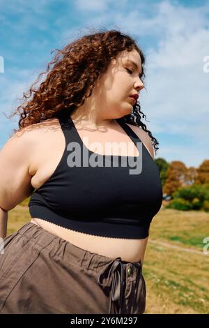 Eine hübsche Frau in Übergröße entspannt sich in einem geräumigen Feld und schätzt die Schönheit der Natur. Stockfoto