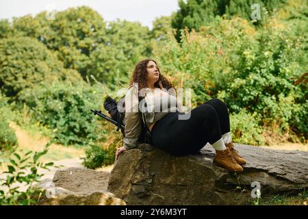 Eine schöne Frau in Übergröße sitzt auf einem Felsen und taucht in das ruhige Ambiente der Natur um sie herum ein. Stockfoto