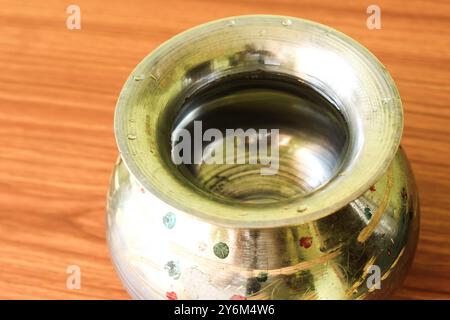 Messingstahlgefäß „Kalash“ (Lota), ein traditioneller kugelförmiger Wasserbehälter, der auf einem braunen hölzernen Hintergrund steht und seine Kultur und seinen Nutzen hervorhebt Stockfoto