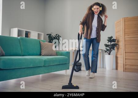 Foto einer charmanten Dame, die in ihrem neuen modernen Loft-Haus drinnen einen Staubsauger für Bodenstaub benutzt und mit Kopfhörern lustigen Disco-Tanz macht Stockfoto