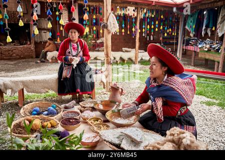 Zwei Frauen in traditioneller Andenkleidung zeigen die Kunst des Webens auf einem lebhaften Chinchero-Markt, umgeben von bunten Garnen und Textilien. Stockfoto