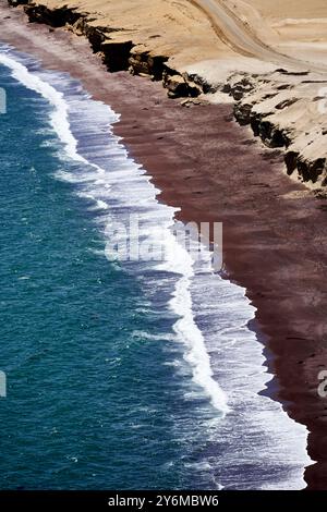 Aus der Vogelperspektive der Wellen, die gegen die felsigen Klippen der Küste von Paracas prallen, und die kontrastreichen Farben und die raue Schönheit der Natur hervorheben. Stockfoto