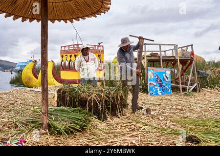 Zwei einheimische Männer auf einer schwimmenden Insel Uros am Titicacasee, die traditionelle Kultur und Lebensstil zeigen. Farbenfrohe handgefertigte Boote und Strukturen Stockfoto