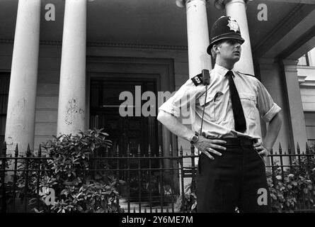 Ein Polizist in Hemdärmeln steht vor der spanischen Botschaft auf dem Belgrave Square in Knightsbridge auf der Wache. Die Polizei wurde nach einem Bombenanschlag ins Gebäude gerufen. Die Eingangstür der Botschaft (im Hintergrund gesehen) zeigt Hinweise auf den Angriff. Eine mit Benzin gefüllte Whiskyflasche explodierte vor der Haustür und verbrannte den Lack. Juli 1969 Stockfoto