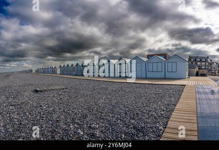 Cayeux-sur-Mer, Frankreich - 09 17 2024: Blick auf farbenfrohe bemalte Strandhütten mit Holzwegen, Kieselsteinen und bewölktem Himmel Stockfoto