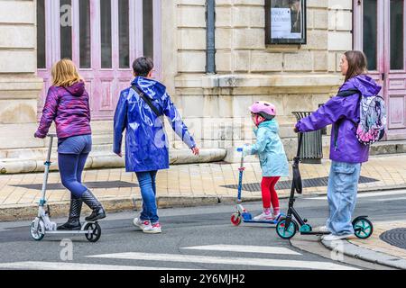 Mutter und drei kleine Kinder auf Rollern/Trottinetten, die die Straße überqueren - Tours, Indre-et-Loire (37), Frankreich. Stockfoto