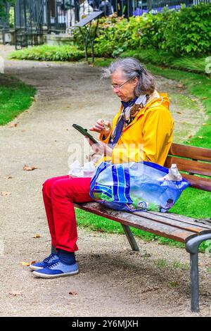 Ältere Frau, die auf der Parkbank im Stadtzentrum sitzt und ihr Smartphone anschaut - Tours, Indre-et-Loire (37), Frankreich. Stockfoto