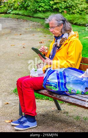 Ältere Frau, die auf der Parkbank im Stadtzentrum sitzt und ihr Smartphone anschaut - Tours, Indre-et-Loire (37), Frankreich. Stockfoto