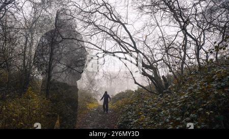 Ein Horrorkonzept. Eine Geisterfigur wie eine Kapuzenfigur, die ein verschwommenes Wesen beobachtet, das einen Pfad hinuntergeht. In einem gruseligen, nebeligen Winterwald. Stockfoto