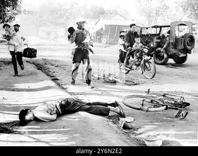 Da Nang, Südvietnam: Sie tragen ihre Kinder in ihren Armen und fahren auf einem Motorrad vorbei vietnamesische Zivilisten passieren die Leiche eines Opfers, das getötet wurde, als der Jeep (rechts) mit südvietnamesischen Regierungstruppen während kommunistischer Angriffe hier am 30. Januar von einem Viet Cong-Terroristen überfallen wurde. Der südvietnamesische Major und sein Fahrer wurden bei dem Angriff getötet. 4. Januar 1968 Stockfoto