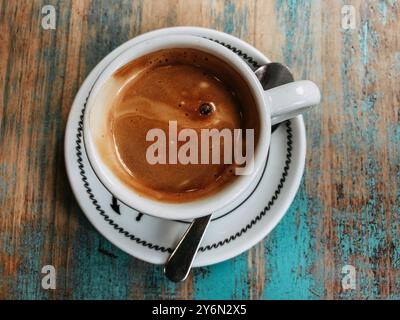Tasse heißer frisch gebrühter Kaffee, Cappuccino, Espresso in weißer Tasse auf blauem, strukturiertem Holztisch. Trinken eines Getränks im Café, im Café. Stockfoto