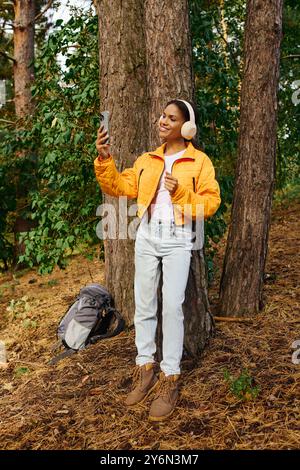 Eine fröhliche junge Frau entspannt sich an einem Baumstamm und genießt ihre Wanderung im wunderschönen Herbstlaub. Stockfoto