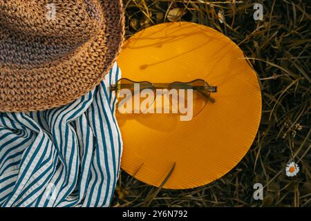 Weibliche Boho-Strohhut und herzförmige Sonnenbrille liegen auf einem gelben Kreis auf einem Rasen. Sommerreisen. Sommer-Ende-Banner. Hallo Herbst. Warmes Licht. Stockfoto
