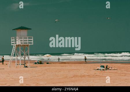 Leerer Strand mit weißer Rettungswache am Horizont am blauen mittelmeer. Holzhütte am morgendlichen Sandstrand. Holzweg führt zum Wasser. Stockfoto