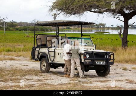 Ein Safariführer und Touristenstand bei einem Jeep im Selous Game Reserve, Tansania. Sie bereiten sich auf ein Wildlife-Abenteuer inmitten üppigen Grüns und offen vor Stockfoto