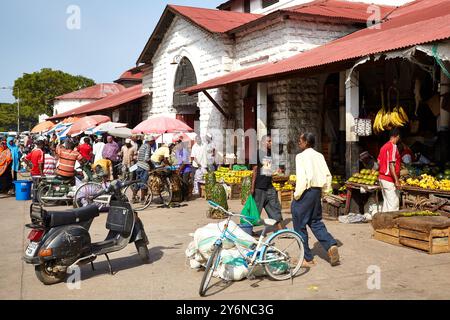 Ein belebter Markt im Freien in Sansibar mit lebhaften Obstständen, verschiedenen Anbietern und lebhaften Interaktionen unter Einheimischen. Die Szene fängt die es ein Stockfoto