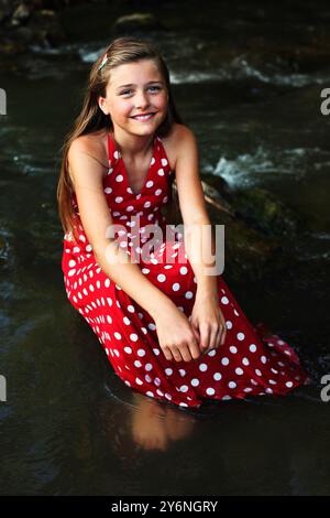 Schönes Mädchen, das auf einem Felsen im Fluss sitzt und lächelt Stockfoto