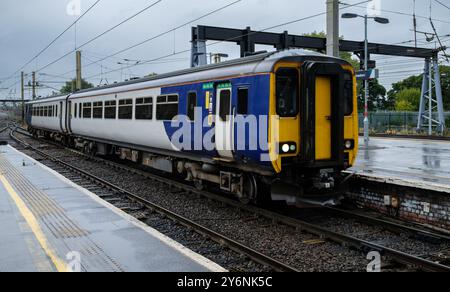 Ein Diesel-Pendlerzug an einem Bahnhof, glänzend unter bewölktem Himmel, bereit für die Abfahrt. Stockfoto