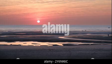 Ruhiger Sonnenuntergang über einem Strand mit reflektierenden Gezeitenpools, die Ruhe und natürliche Schönheit wecken. Stockfoto